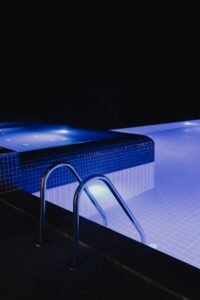 A steel handrail with blue tiled illuminated pool at night, creating a serene and modern ambiance.
