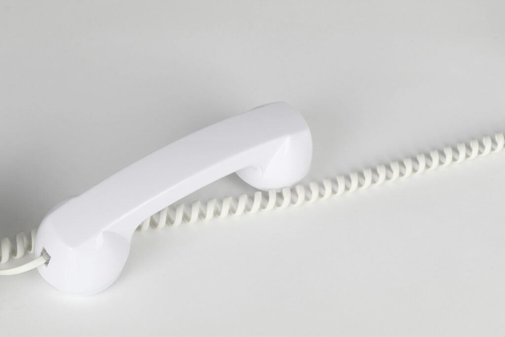 Simple and elegant close-up of a white corded telephone handset on a white background, emphasizing minimalism.